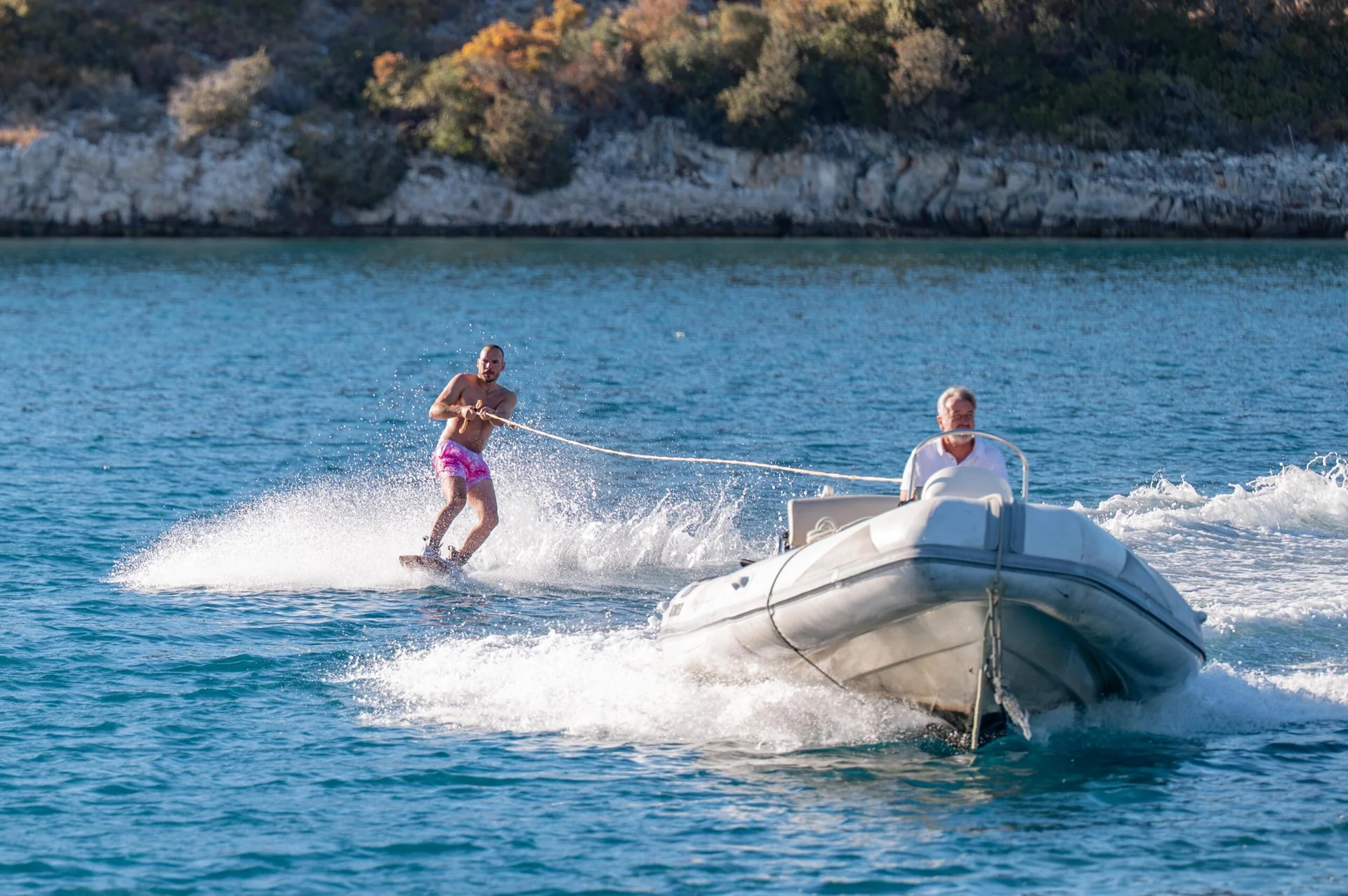 PACHA A man wakeboarding behind a motorboat on a calm sea.