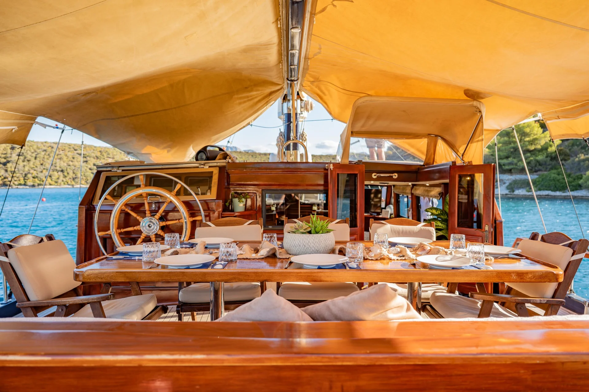 PACHA A wooden dining table set for a meal on the deck of a boat, positioned under a yellow canopy.