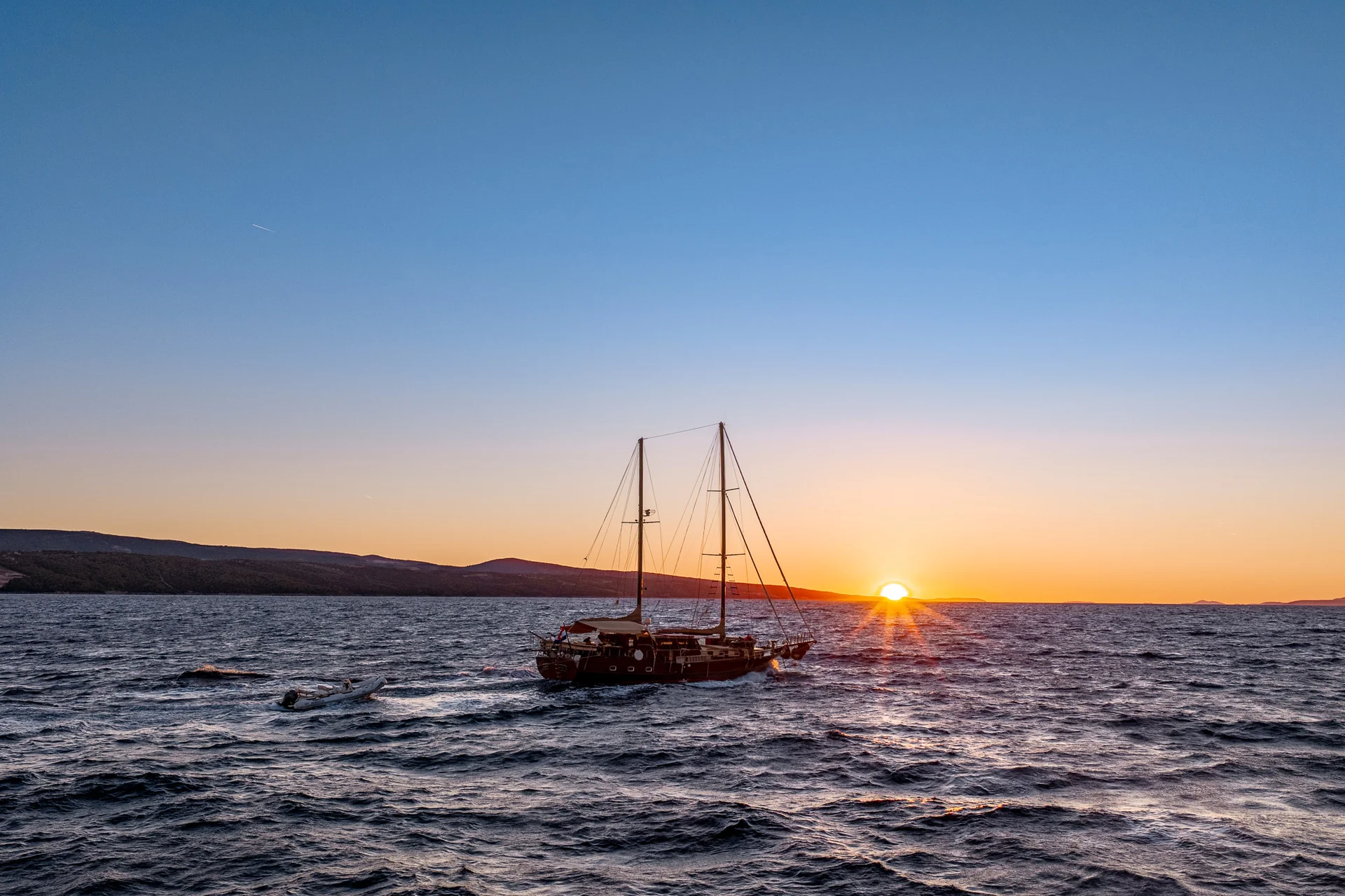 PACHA A sailboat on the water at sunset with a small motorboat trailing behind.