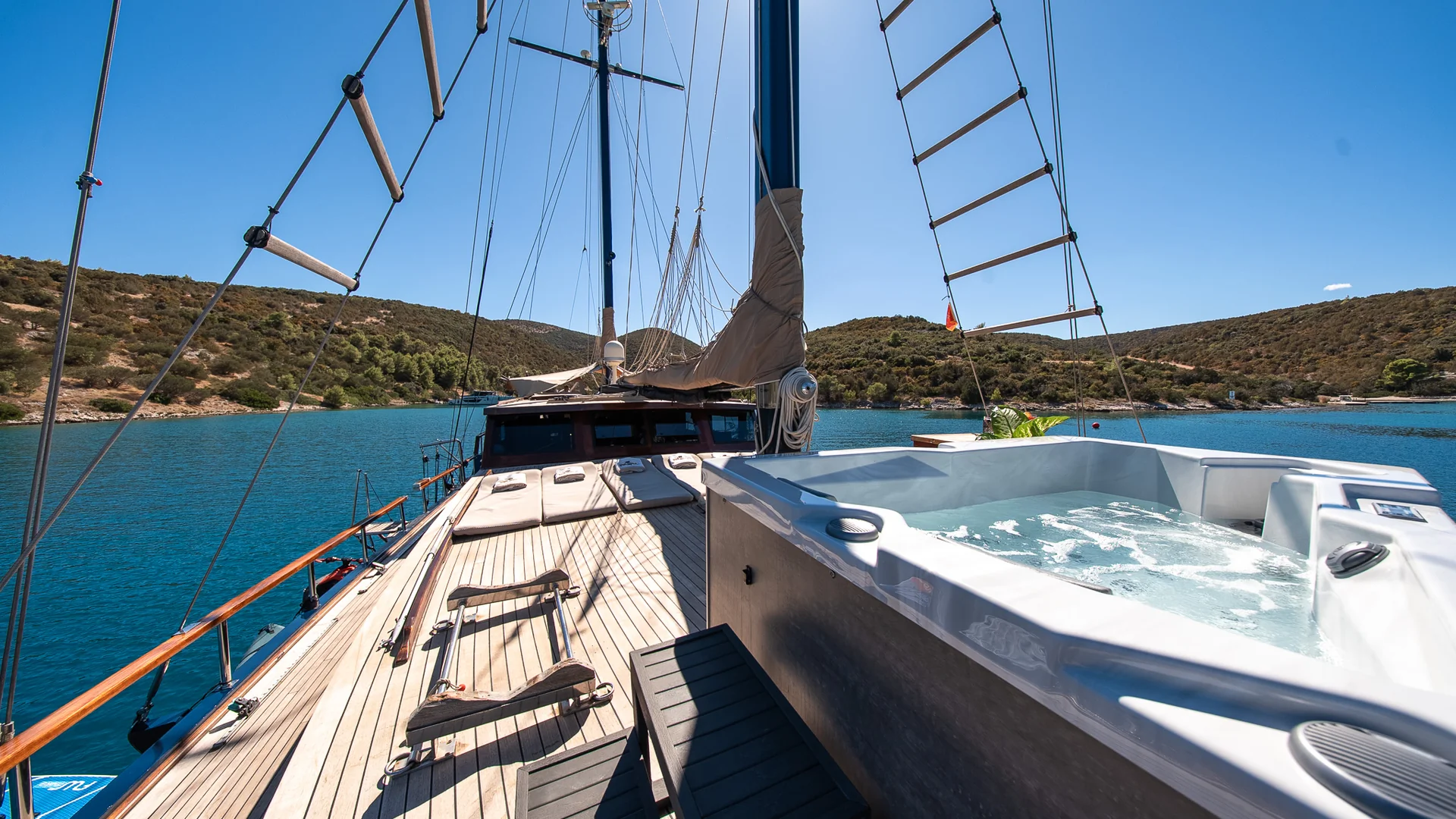 PACHA A hot tub on the deck of a wooden sailboat, overlooking a calm bay surrounded by hills.