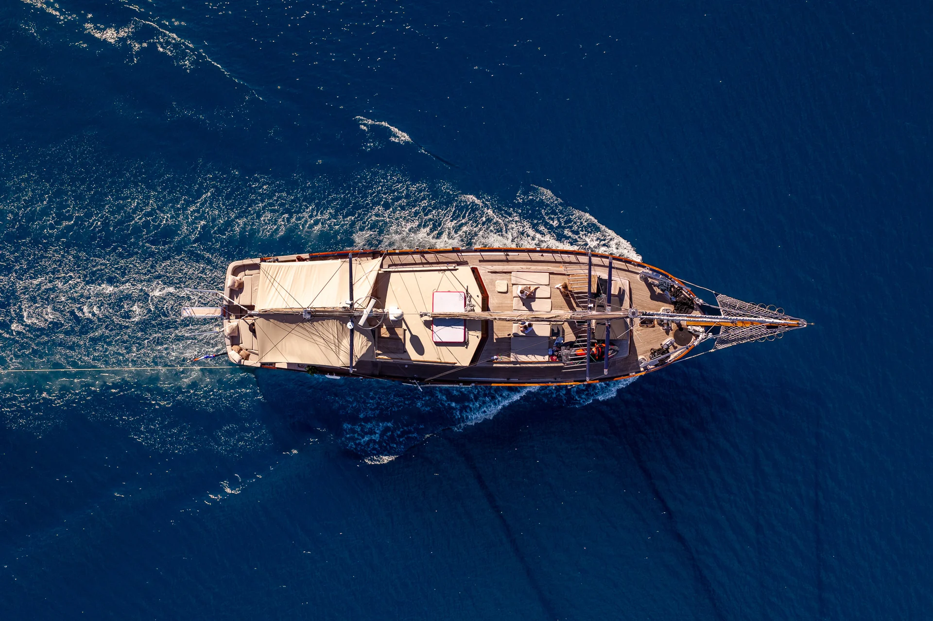 PACHA Aerial view of a wooden sailboat moving through deep blue water.