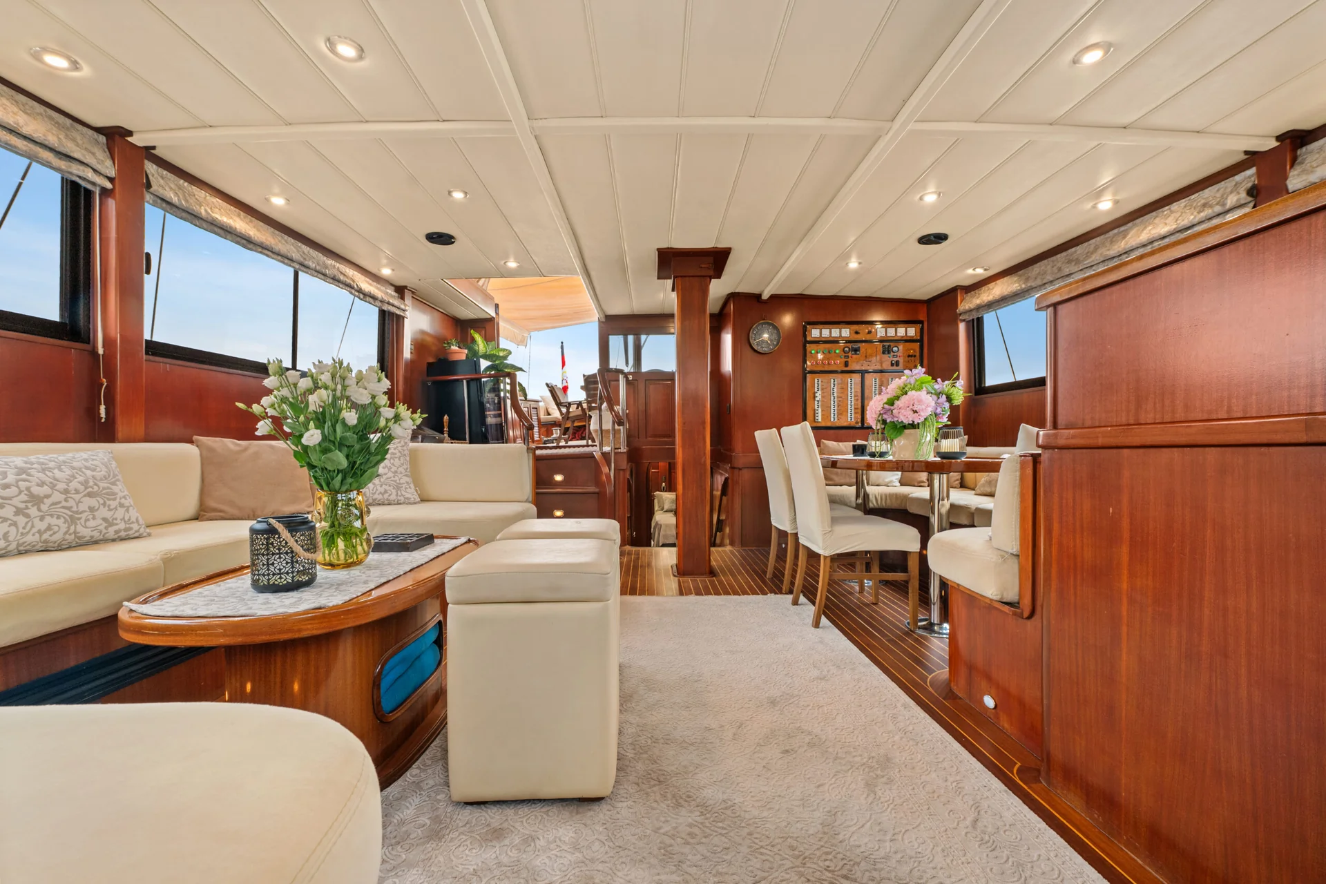 PACHA Interior of a yacht salon featuring a cream-colored sofa, a wooden coffee table with a flower vase, and a dining area with four chairs around a circular table.