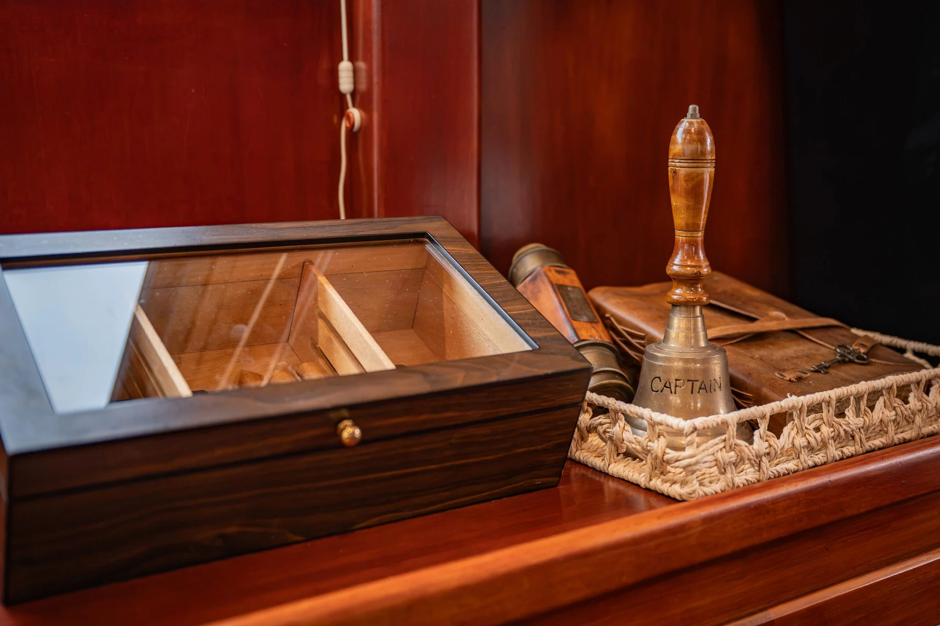 PACHA A wooden humidor, a bell with CAPTAIN engraved on it, and a leather case sitting on a wooden surface.