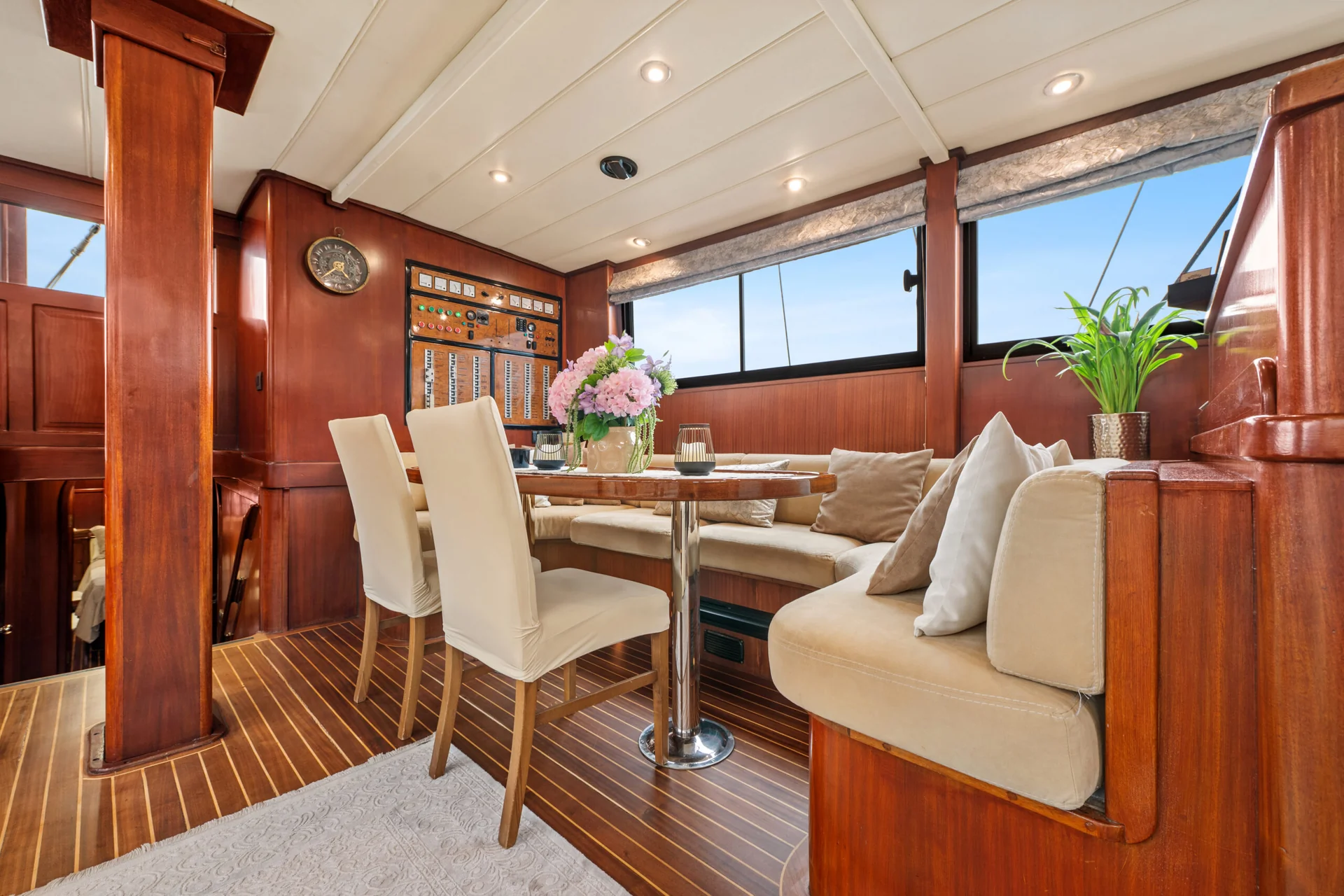 PACHA Dining area inside a wood-paneled boat cabin with a circular table, two chairs, and built-in bench seating.