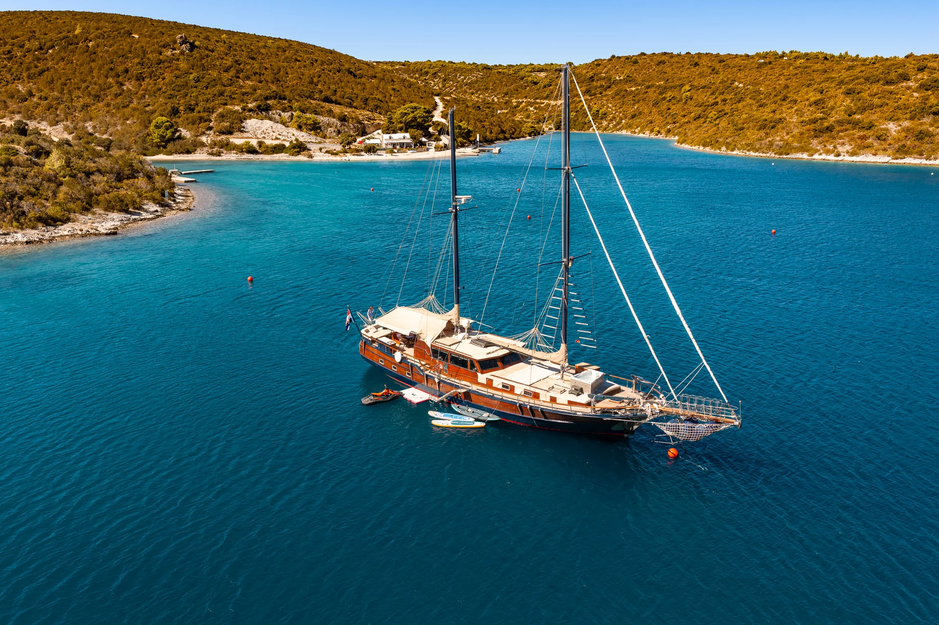 PACHA A wooden sailing yacht anchored in a turquoise bay surrounded by hills.