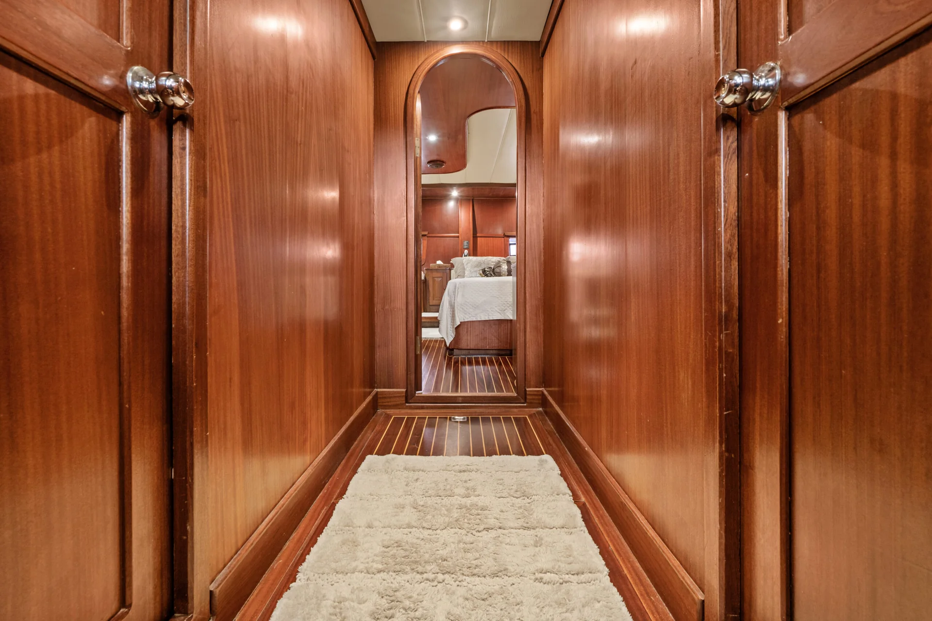 PACHA Narrow wooden hallway with an arched doorway leading to a bedroom featuring a bed with white linens.
