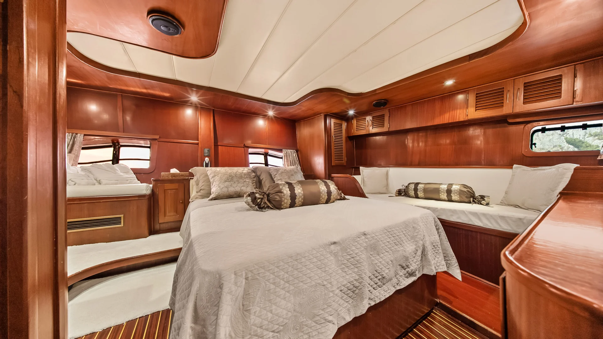 PACHA The interior of a yacht cabin featuring a central bed with a quilted cover, flanked by two built-in bench seats with cushions against warm wood-paneled walls.
