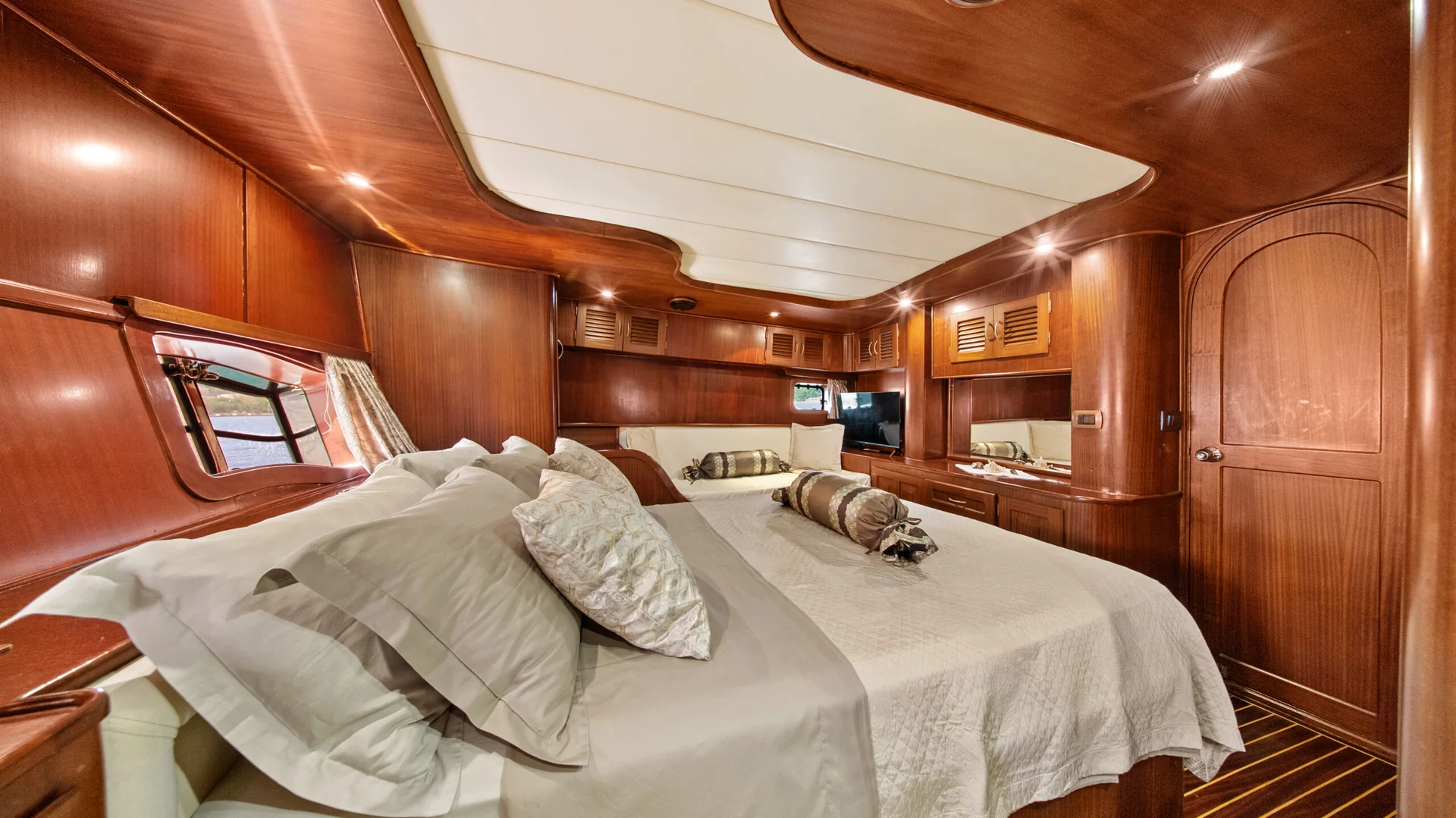 PACHA The interior of a wood-paneled yacht cabin featuring a large bed with neutral bedding and a small sofa in the background.