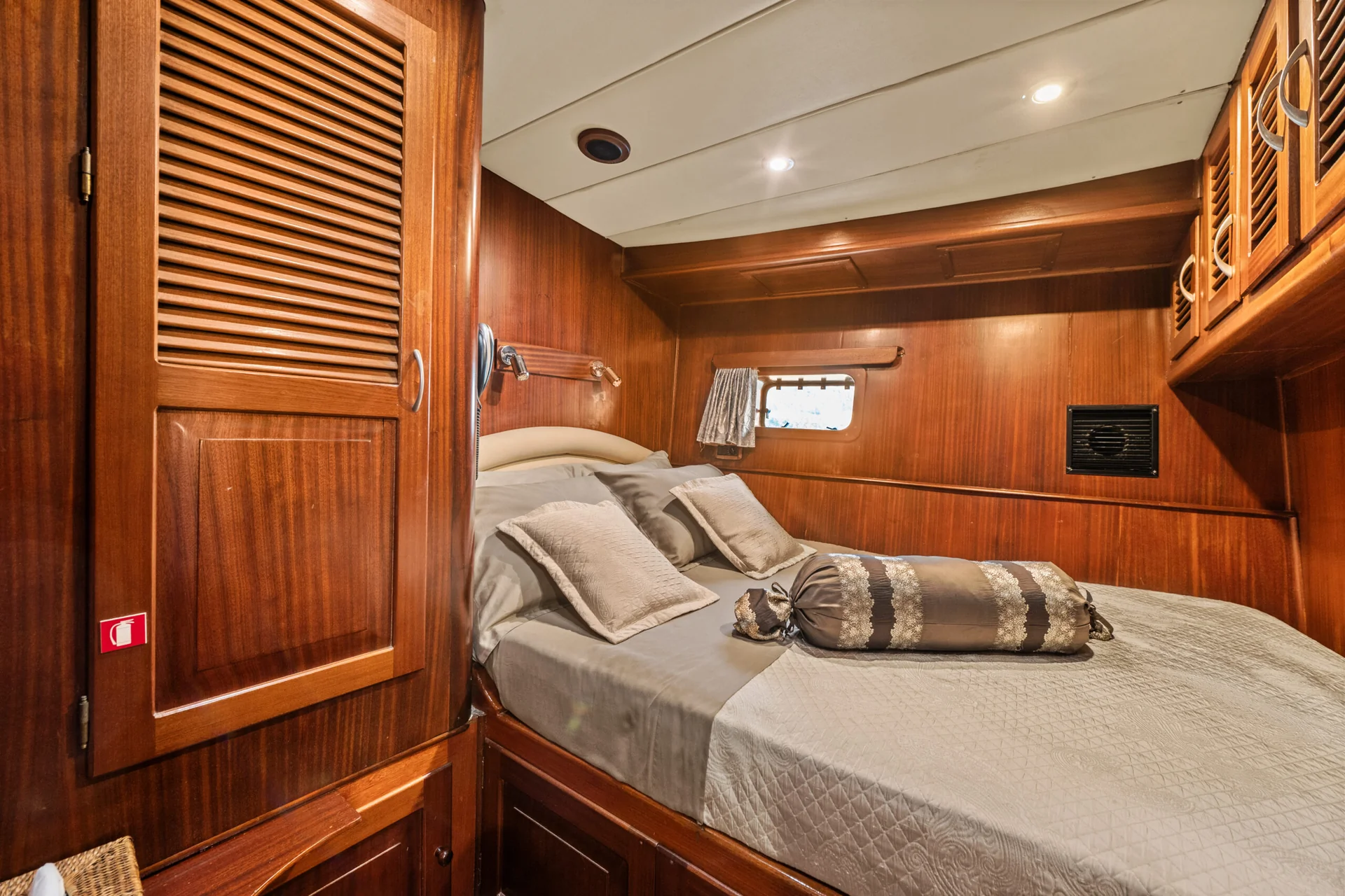 PACHA Small cabin with wood paneled walls, a double bed with decorative pillows, and a large louvered closet door.