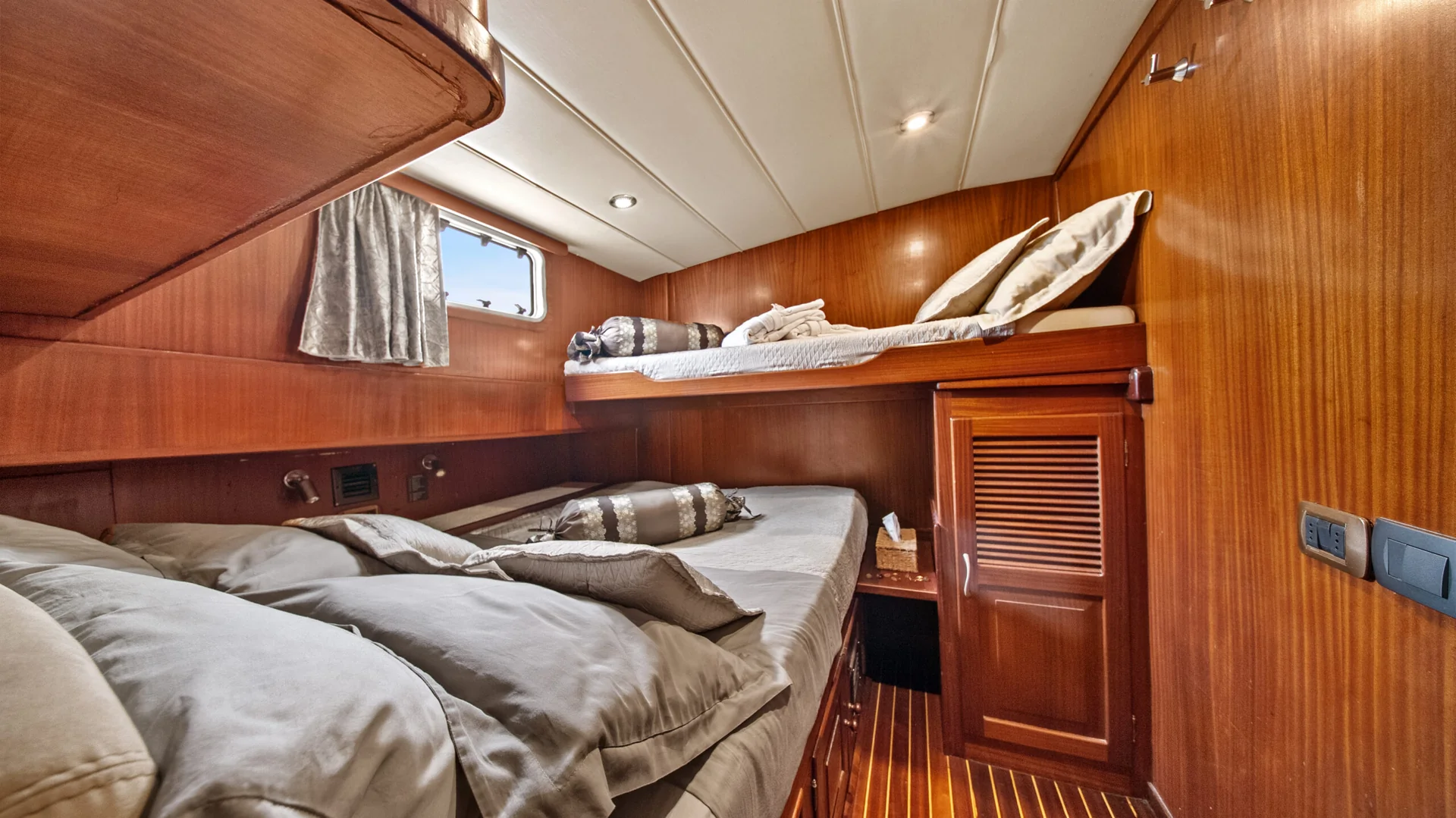 PACHA A ship cabin featuring a lower double bed and an upper bunk bed, both with pillows and wood paneling.