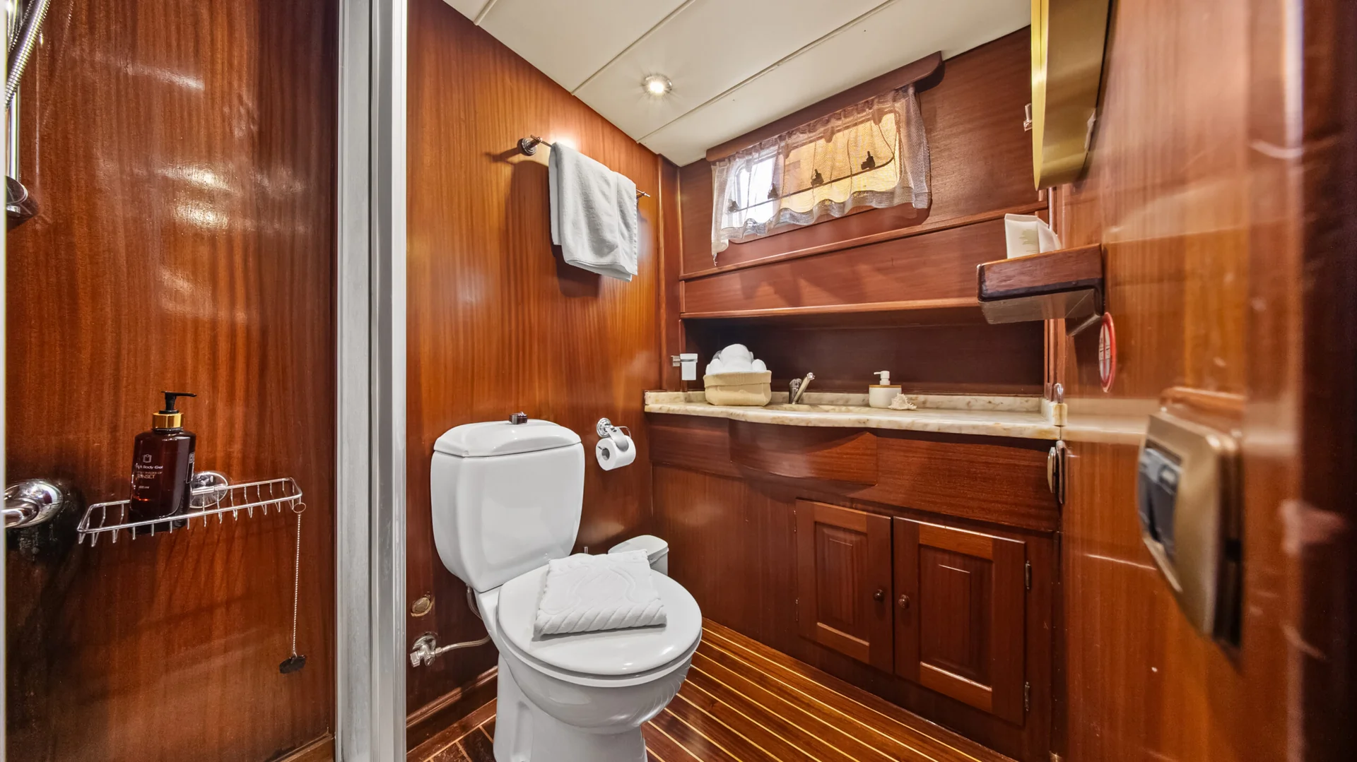 PACHA Small boat bathroom with wood paneling, a white toilet, and a sink basin set into a wooden vanity.
