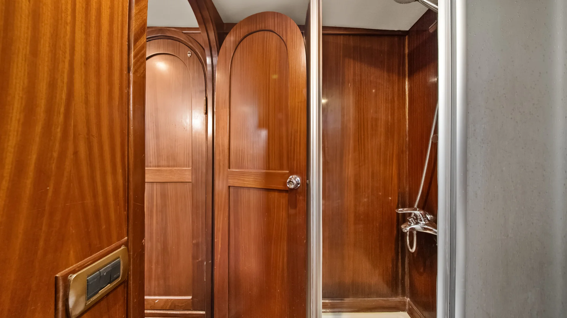 PACHA Interior of a bathroom with high-gloss wood paneling and arched wooden doors, featuring a metal shower head and faucet.