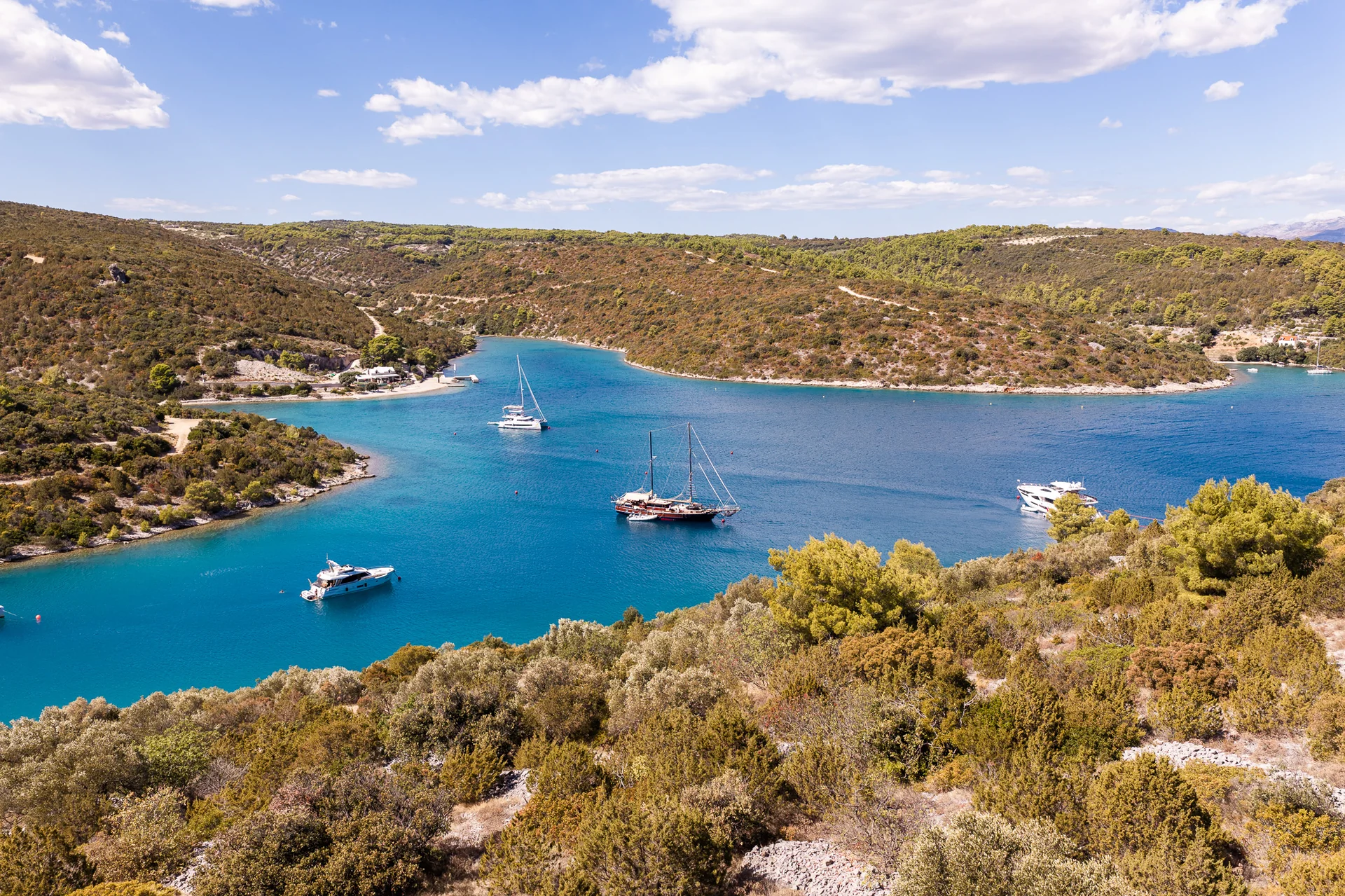 PACHA Several yachts anchored in a sheltered blue bay surrounded by hilly, scrub-covered coastline.