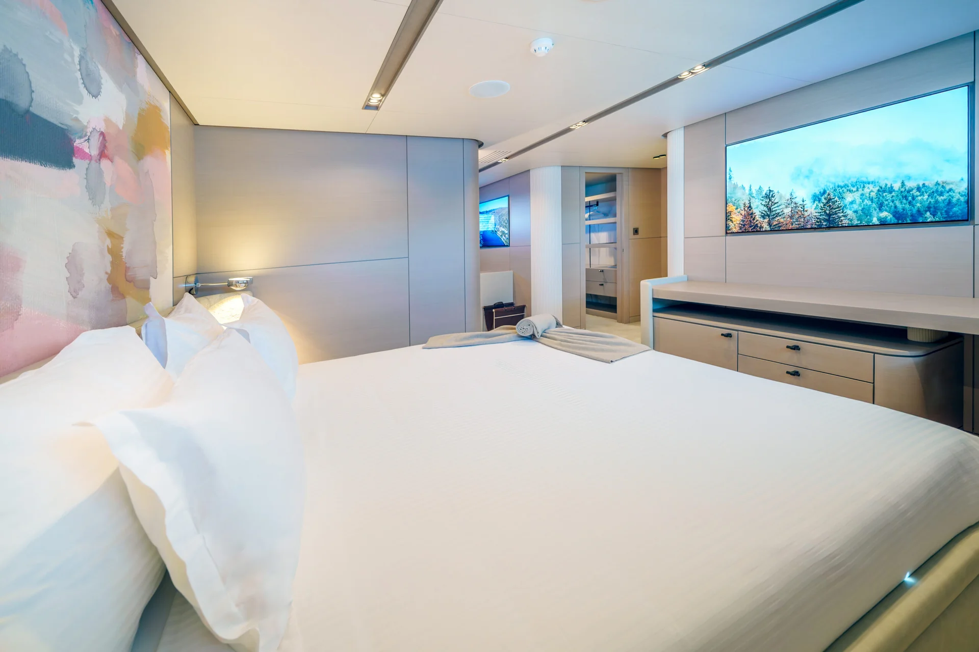 ORIY Modern bedroom with a large bed, white linens, abstract wall art, built-in cabinets, TV, and soft lighting creating a clean and inviting atmosphere.