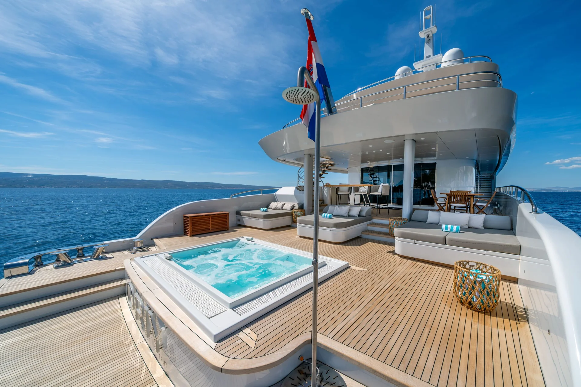 ORIY A luxurious yacht deck with a hot tub, lounge chairs, a shower, and modern seating, overlooking a calm blue sea under a clear sky.