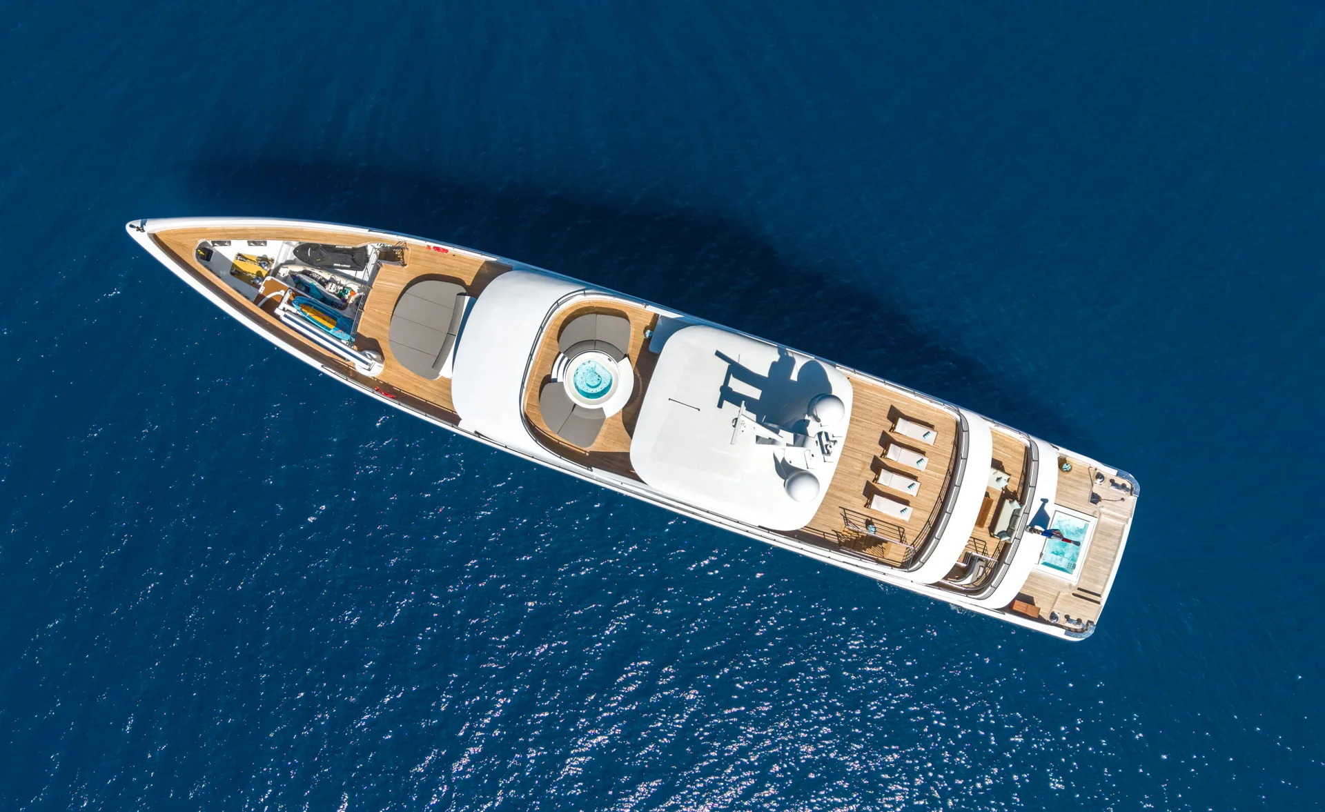 ORIY Aerial view of a large luxury yacht with a pool on deck, floating on calm, deep blue water.