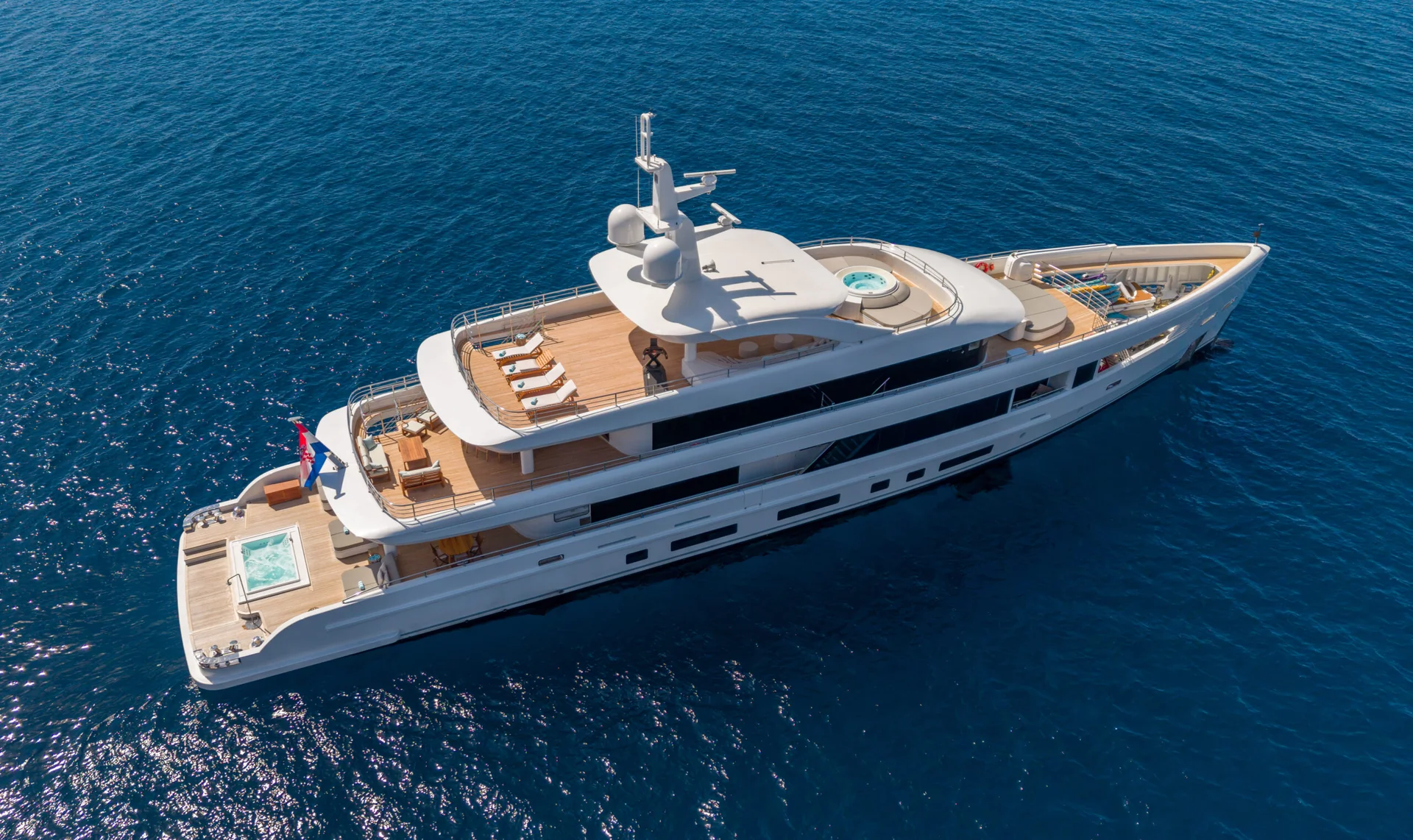 ORIY A large white luxury yacht with two decks, several lounge areas, and small pools at the front and back, floating on calm, deep blue water.