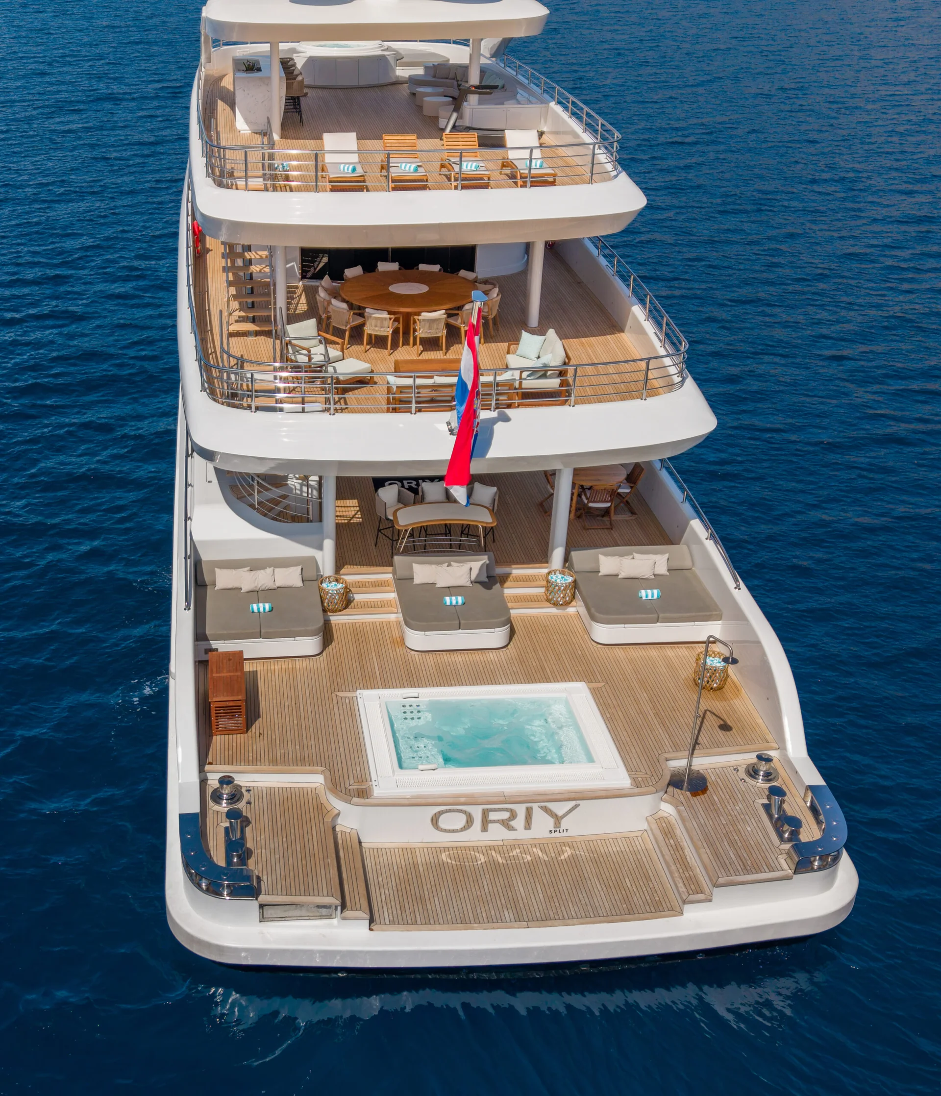 ORIY A luxury yacht with multiple decks, sun loungers, a small pool, and a Norwegian flag sails on calm blue water. The name ORIY appears on the lower deck.