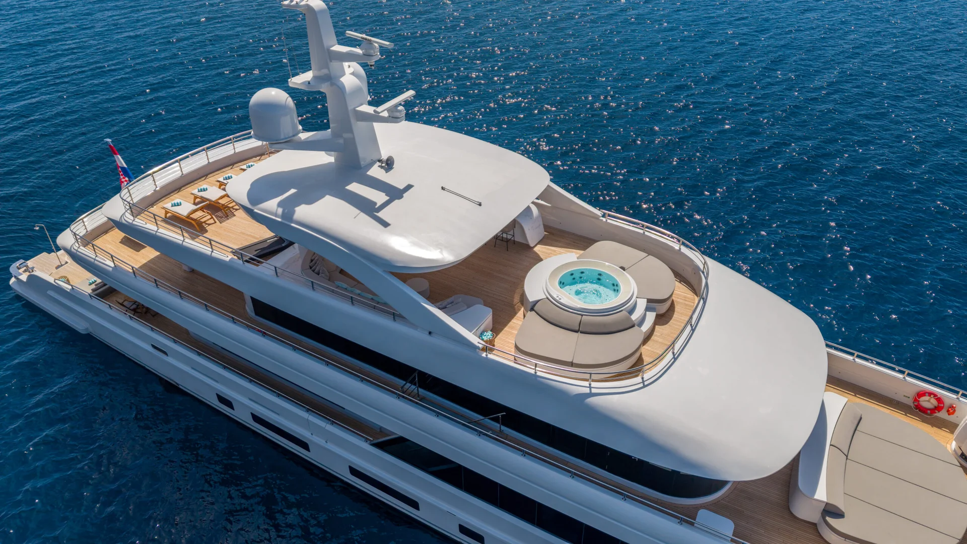 ORIY A luxurious white yacht with a hot tub on its upper deck cruises on calm blue water under the sun.