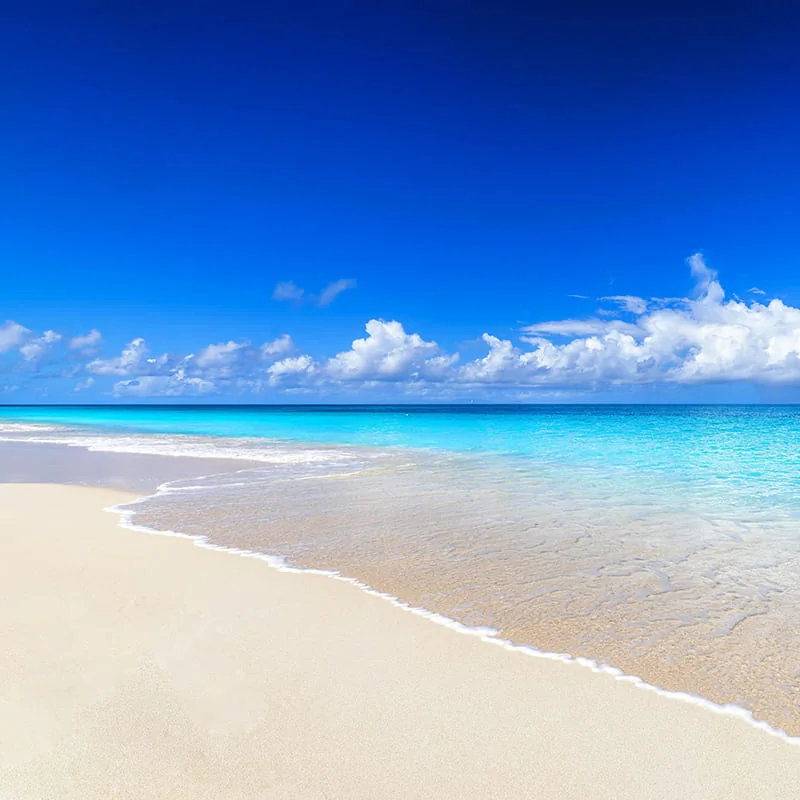 A serene beach with clear turquoise water, white sand, gentle waves, and a bright blue sky with fluffy white clouds.