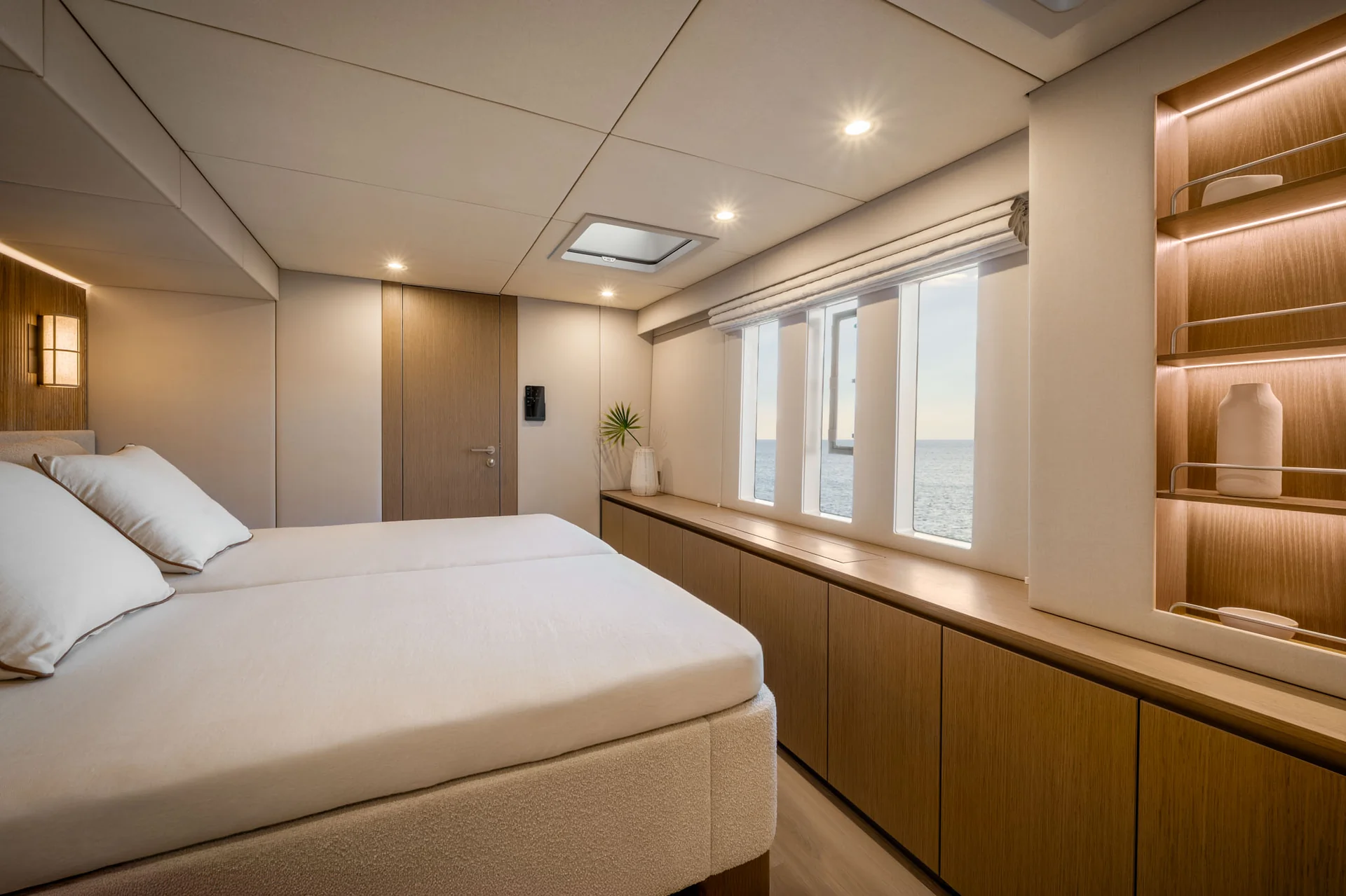 Modern yacht cabin with a bed, light wood cabinetry, and a window view of the ocean.