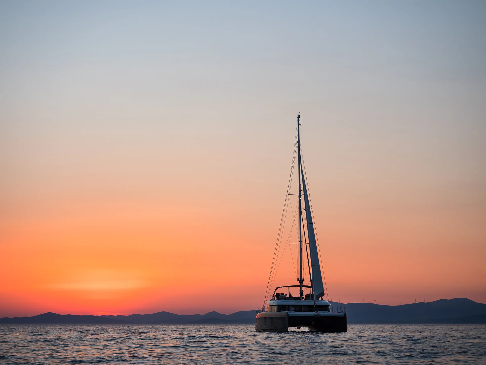 A sailboat on the water at sunset with distant hills in the background.