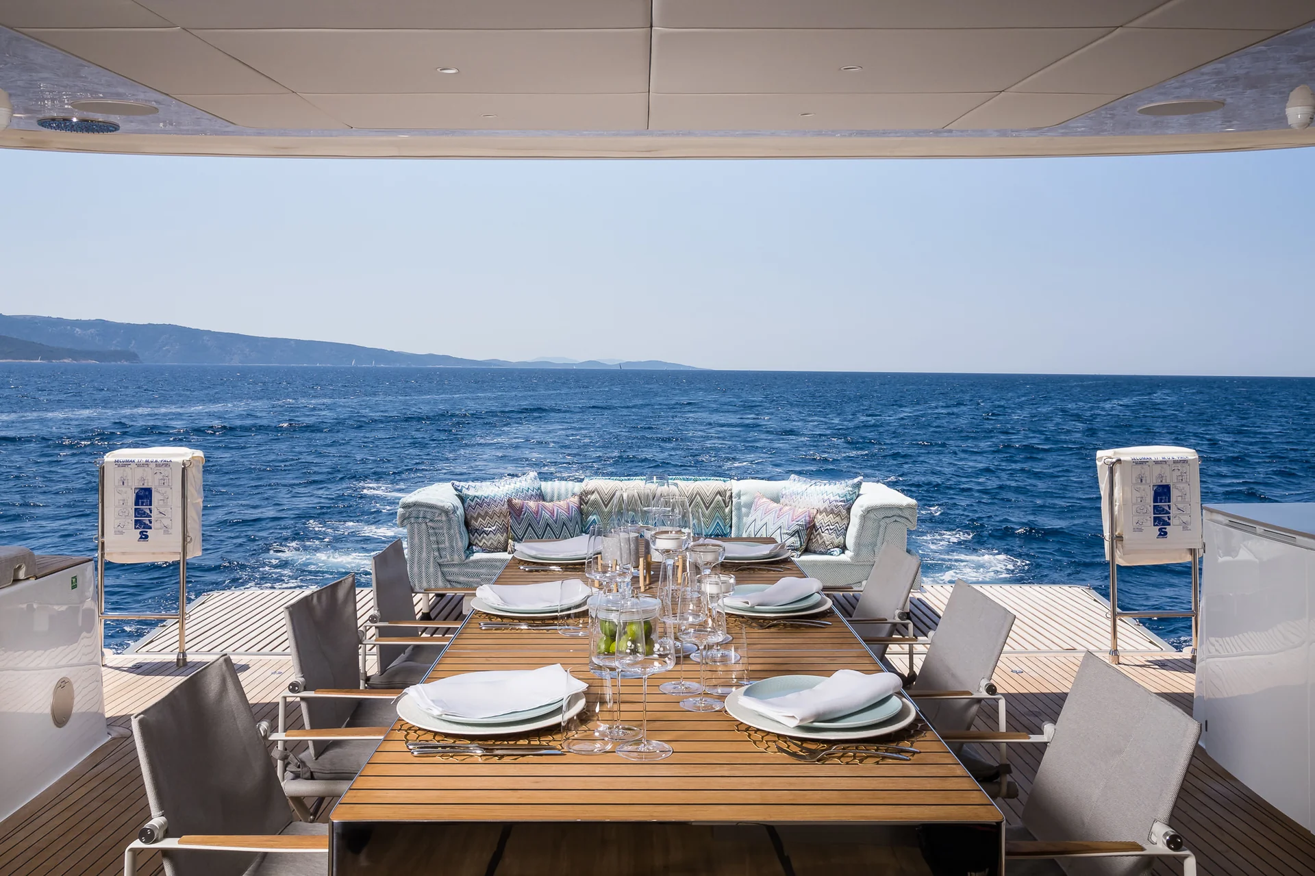 Dining table set for a meal on the deck of a yacht overlooking the ocean.