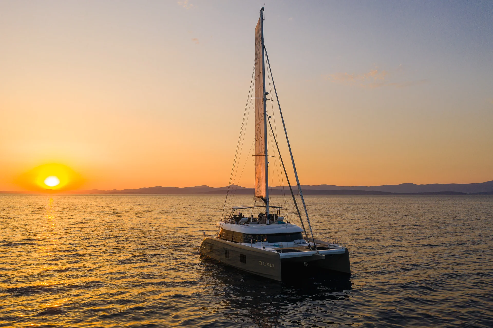 A catamaran sailboat on the ocean during a golden sunset.