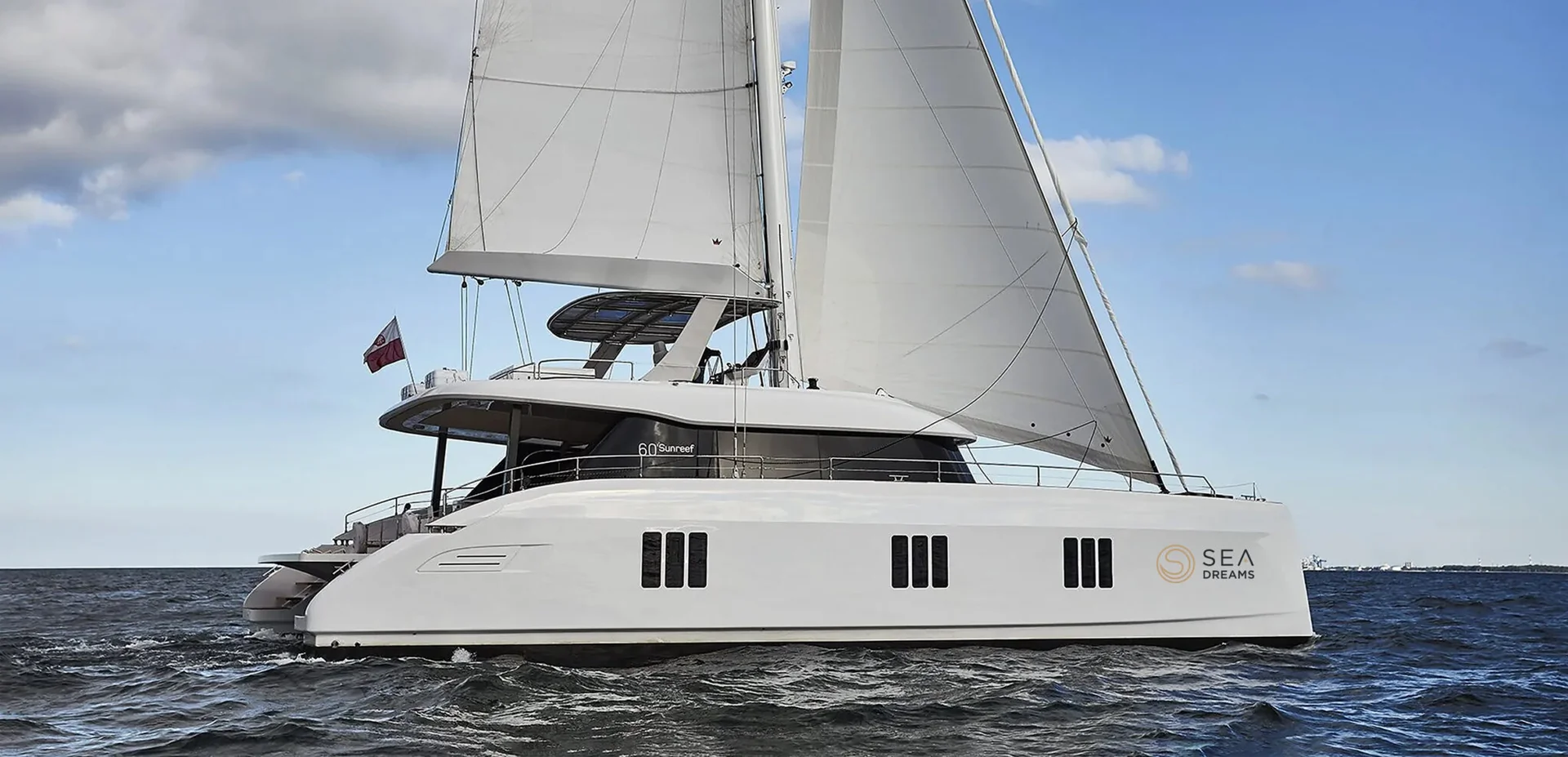 A white Sunreef 60 catamaran sailboat named Sea Dreams sailing on the open ocean.