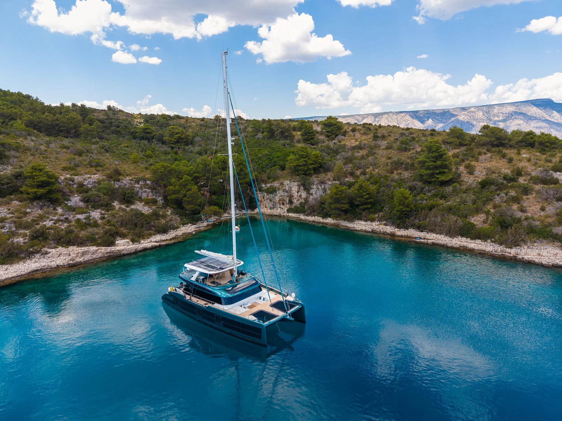 A catamaran anchored in a clear blue cove surrounded by a rocky, forested coastline.