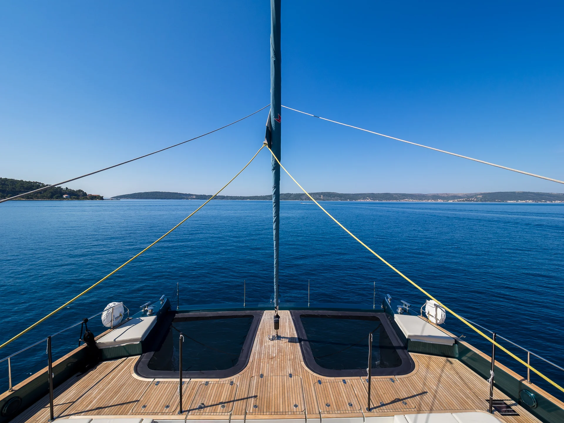 View from the deck of a catamaran looking forward over the calm blue sea toward distant land.