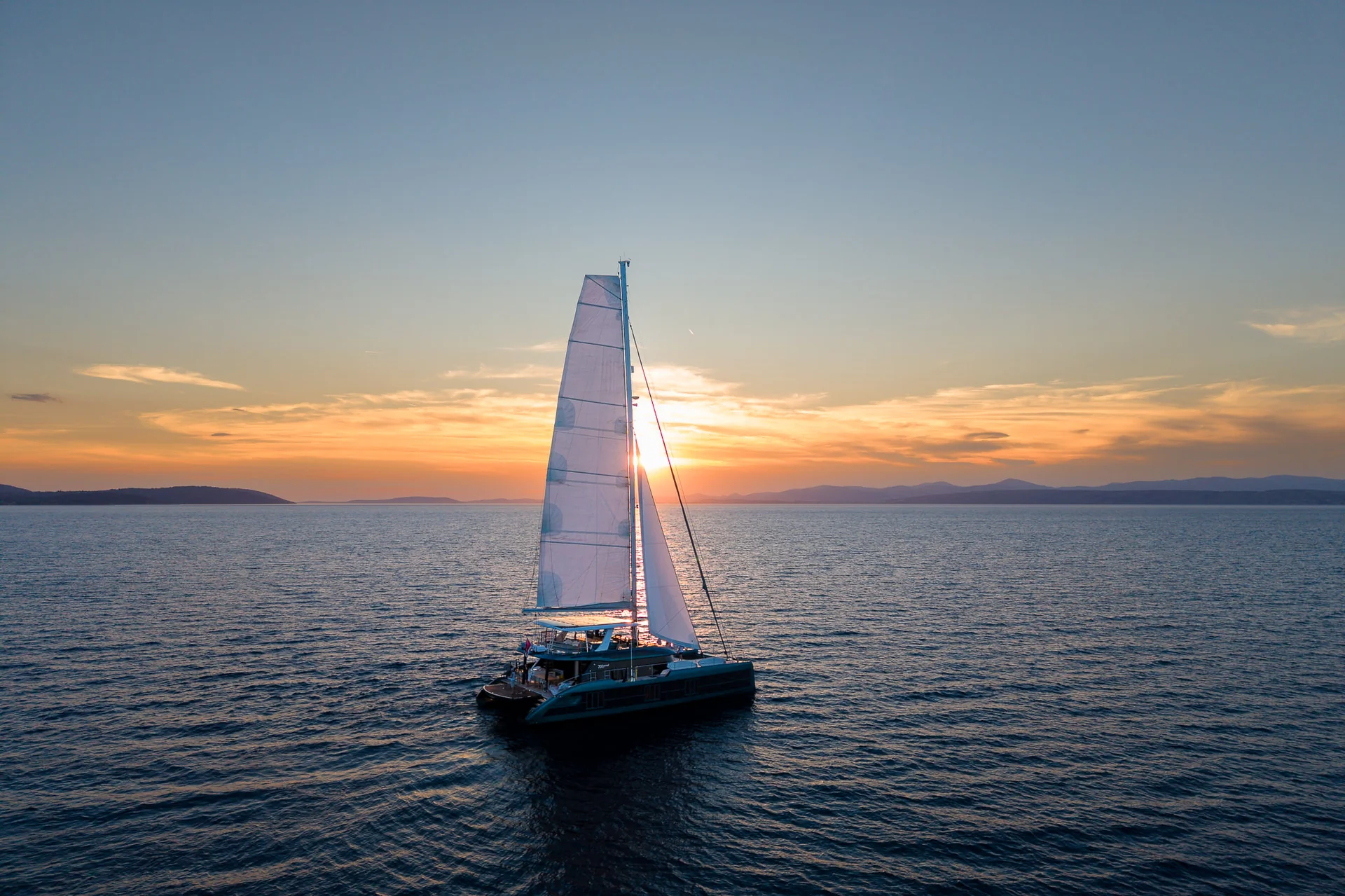 A catamaran sailing on the open sea during a sunset.