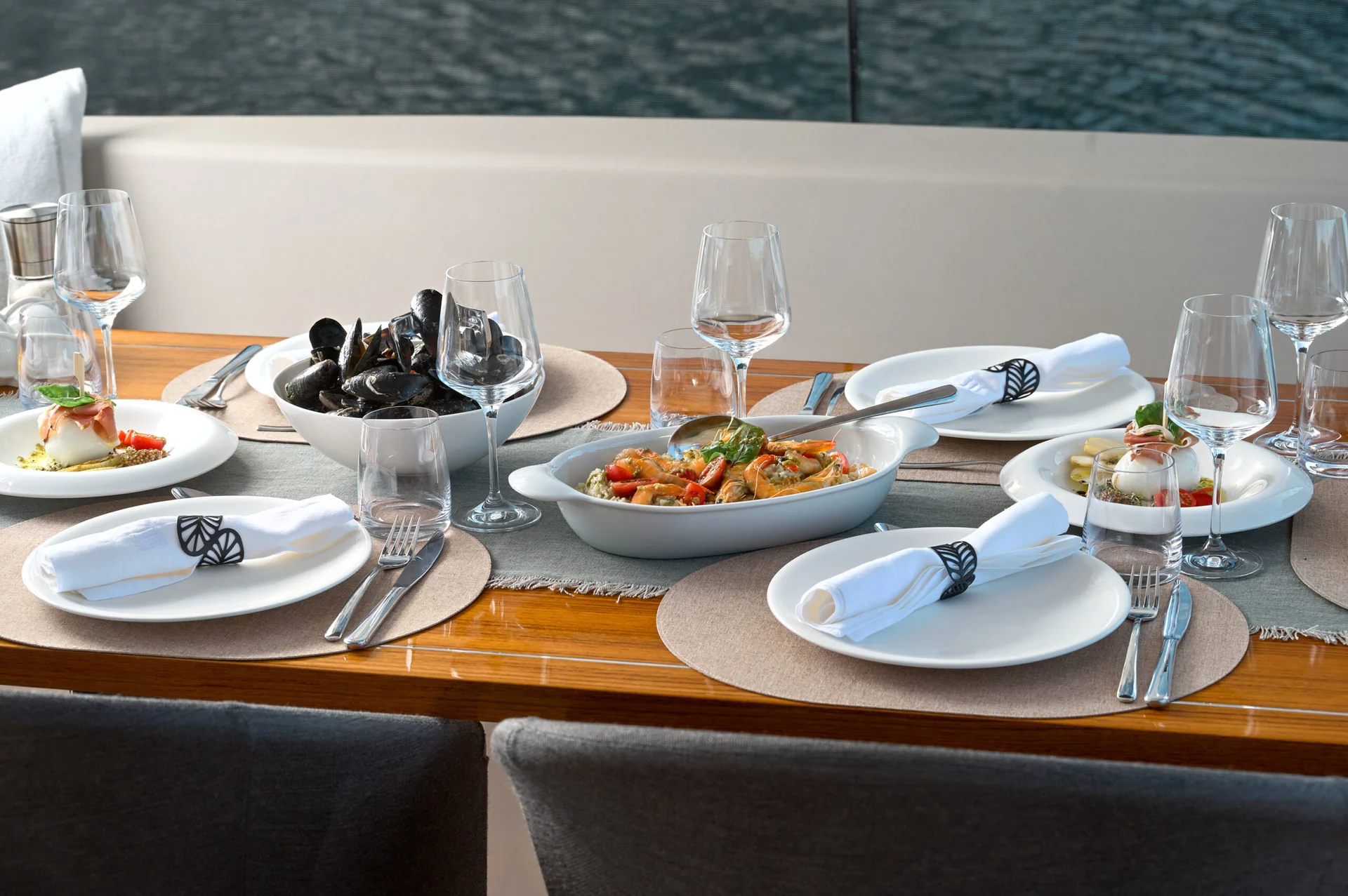 A table set for four on a boat, featuring a bowl of mussels, a dish of shrimp, and plates with appetizers.