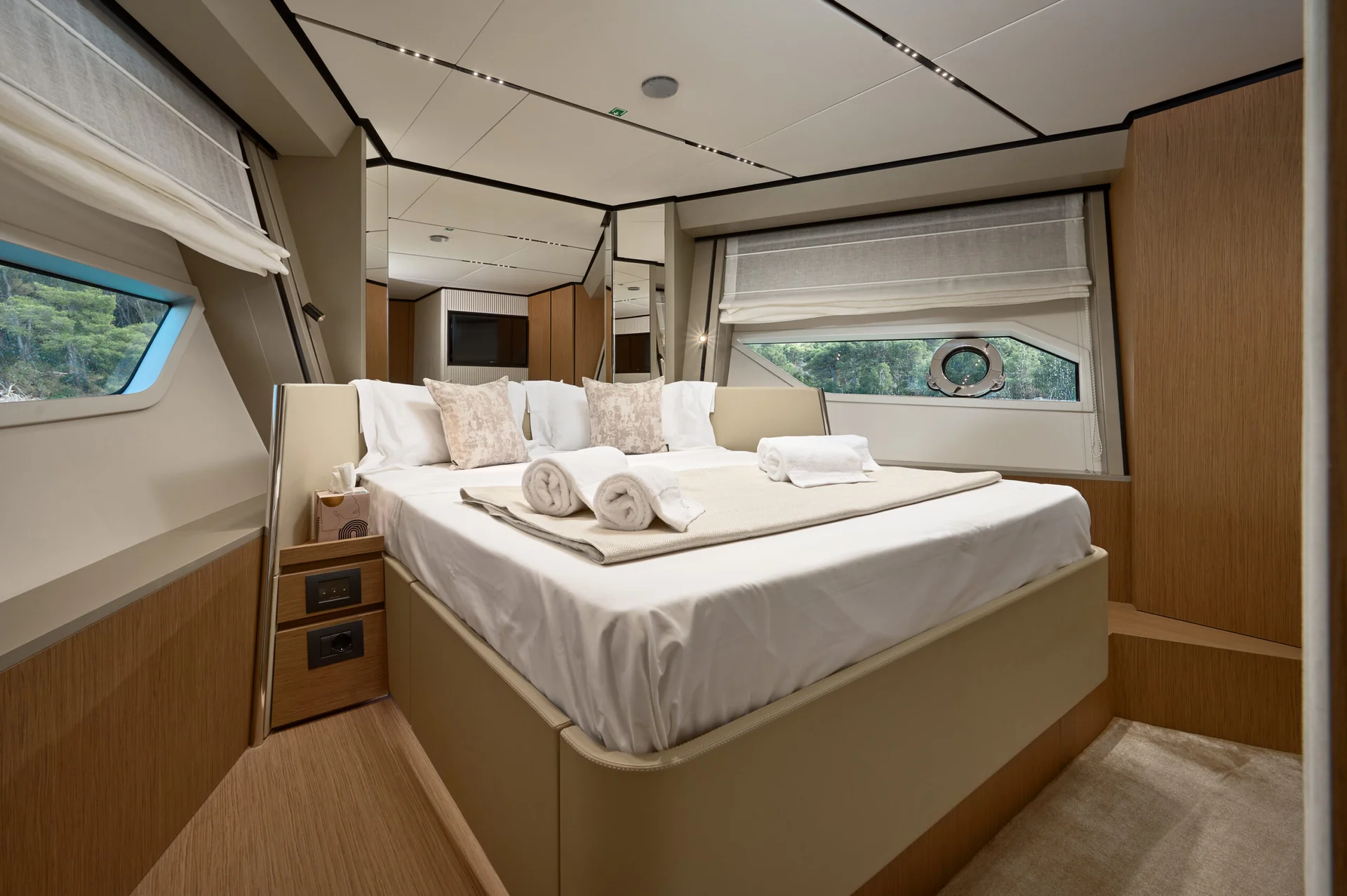 A made queen bed with two rolled towels on top in a wood-paneled yacht stateroom.