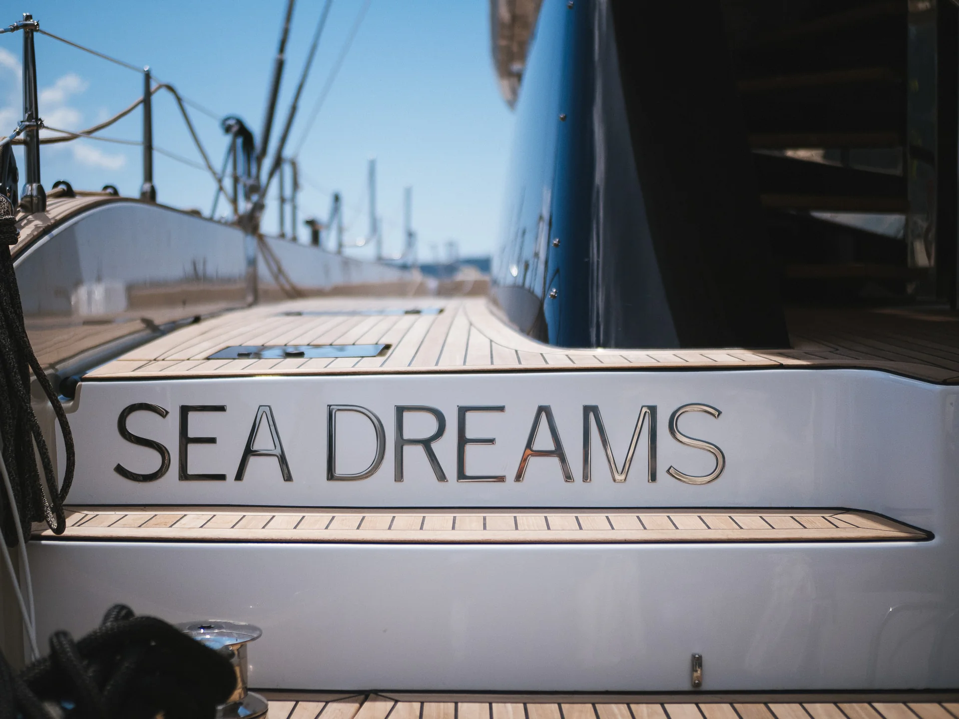 The name SEA DREAMS in silver lettering on the white stern of a yacht with a teak deck.