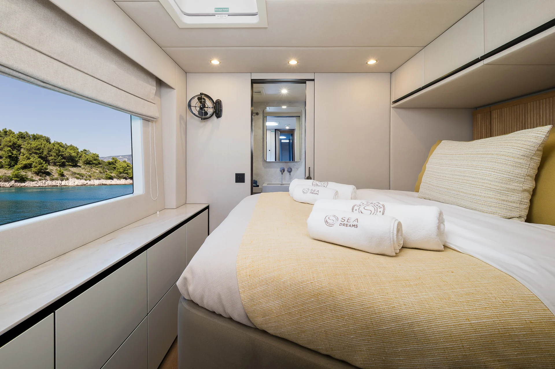Interior of a yacht cabin featuring a bed with folded towels, a window overlooking the sea, and an open doorway to a bathroom.