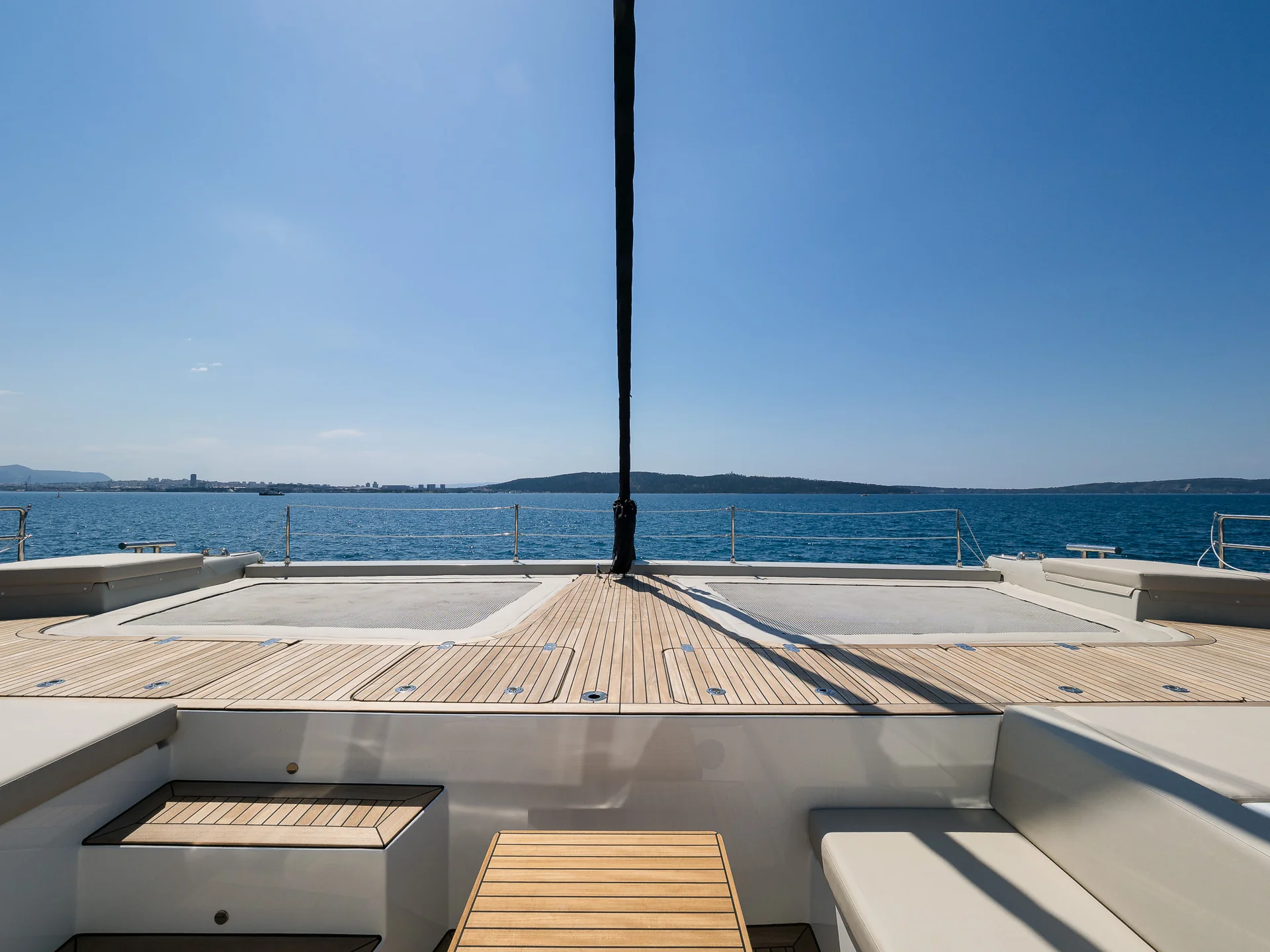 View from the deck of a catamaran looking out over the open sea toward a distant coastline.