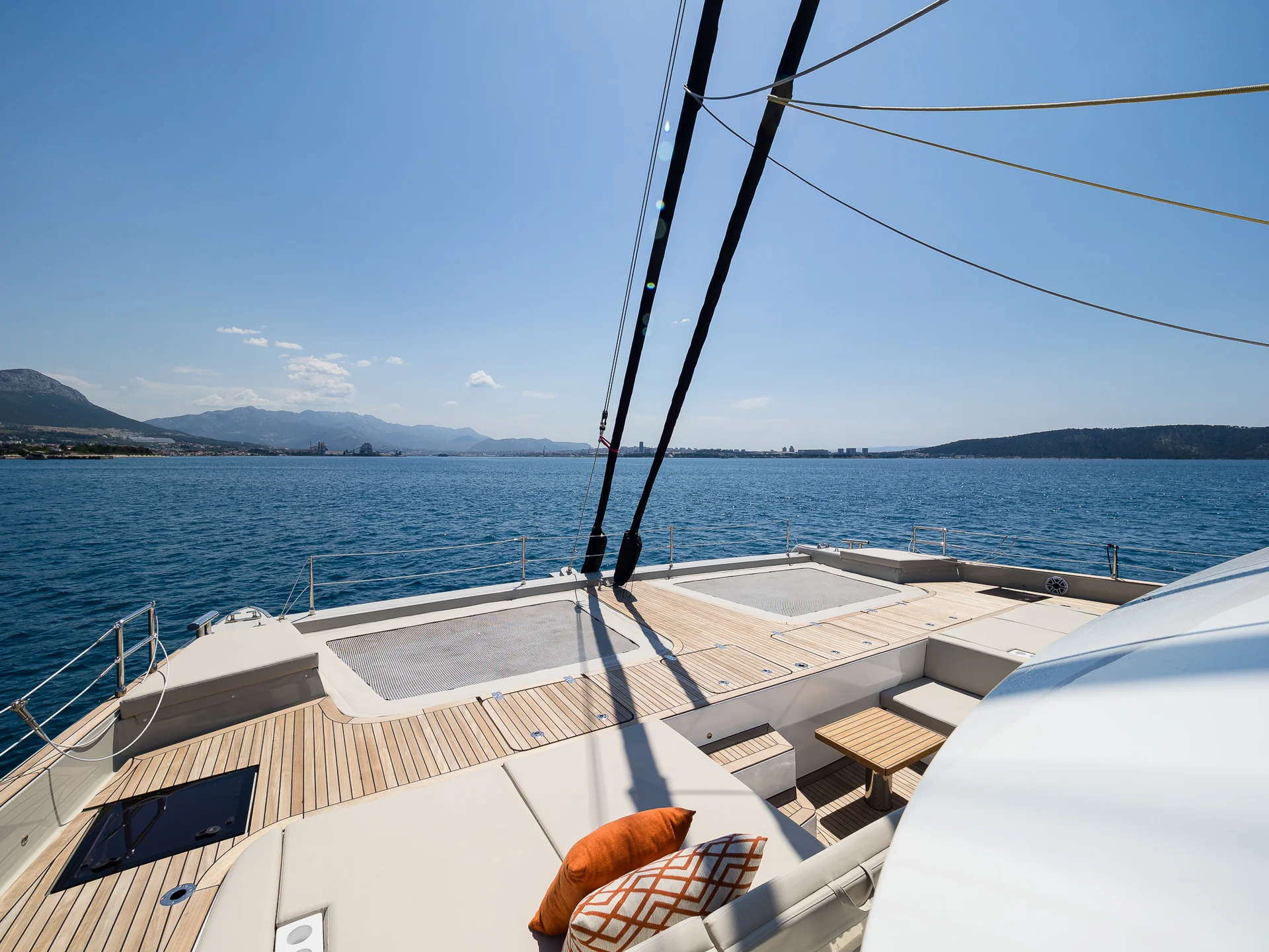 View from the deck of a catamaran looking out over the open sea toward a distant coastline under a clear blue sky.