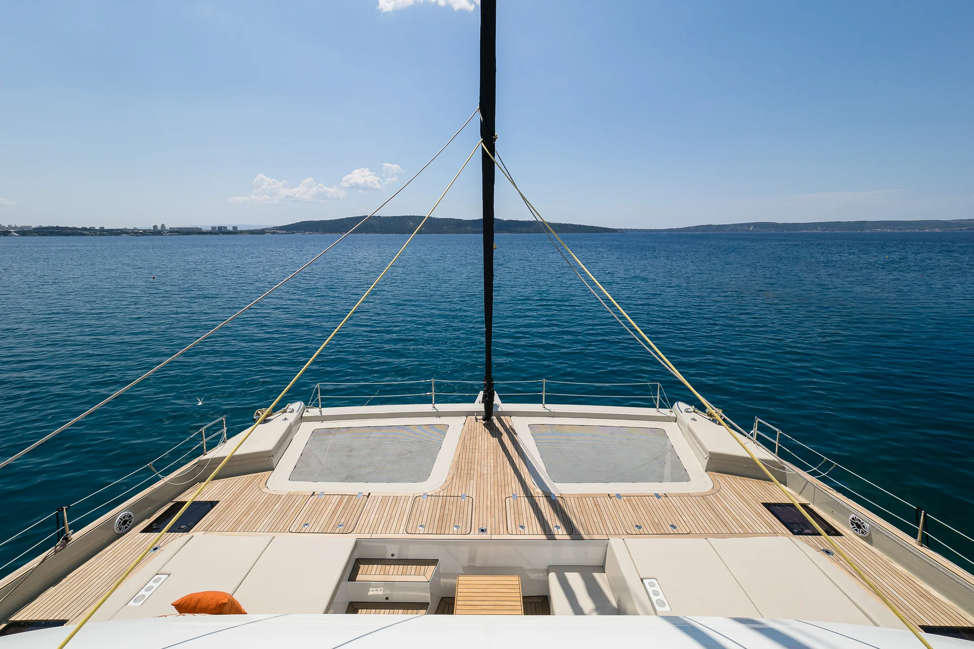 View from the bow of a catamaran looking out over the open sea towards a distant coastline.